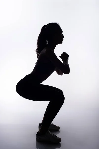 Silhouette slim body of Young Fitness Woman squad her legs for exercising in full body length. High contrast white background copy space