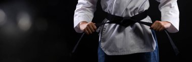 Ulusal sporcu olan Kara Kemer Tekvando Karate Kız geleneksel dövüş pozları veriyor. Spor üniformalı yumruklar, izole siyah arka plan, ayak parmaklarında hareket bulanıklığı