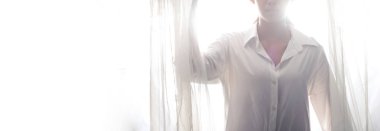 Genç Asyalı kız perdenin penceresinden rüzgar ve güneş ışığı ile uyanır. Sabah vakti kendini mutlu hisseden bir kadın. yüksek tuş pozlama, kopyalama alanı