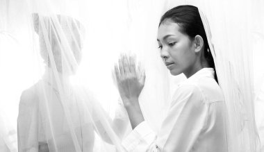 Genç Asyalı kız rüzgârla uyanır ve perdenin arkasından güneş ışığı gelir. Kadın sevgilisinin elini tutar. Gölgede ve rüyada. yüksek tuş pozlama, kopyalama alanı