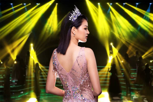 Portrait of Miss Pageant Beauty Contest in Pink sequin Evening Ball Gown with Diamond Crown, Asian Woman turn half face as unrecognized person over stage and light background