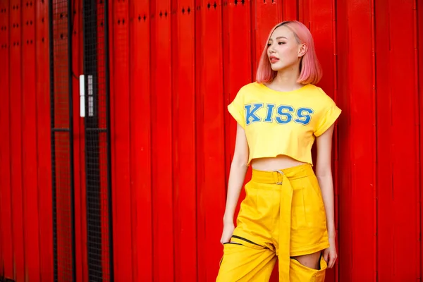 街上的时尚女人穿着黄色时髦的衣服 一头垂死的粉色头发 年轻姑娘把浓郁的红色彩墙艺术装扮成夏天的流行风格 复制空间 — 图库照片