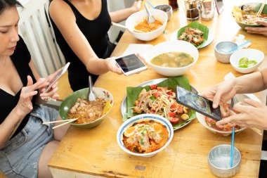 Kızlar, Spicy Street Food, Noodle Tomyum baharat çorbasını sosyal medyaya yüklemeden önce akıllı telefonlu Lezzetli ve güzel görünümlü yiyeceklerle fotoğraf çekiyorlar.