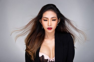 Moda güzeli kadının uzun düz sarı saçları vardır. Kameraya bakar ve duygularını ifade eder. Asyalı bir kızın portresi gri arka plan üzerine siyah bir elbise giyer.