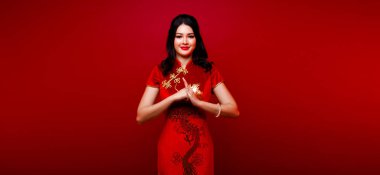 Moda güzeli kadının uzun düz siyah saçları vardır. Kameraya bakar ve kutlama yapar. Asyalı kızın portresi kırmızı arkaplan üzerine kırmızı Çin elbisesi giyer.