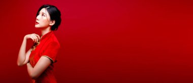 Moda güzeli kadının uzun düz siyah saçları vardır. Kameraya bakar ve kutlama yapar. Asyalı kızın portresi kırmızı arkaplan üzerine kırmızı Çin elbisesi giyer.