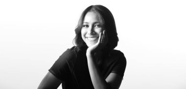 Güzellik Kadını 'nın düz siyah saçları ve mutlu bir gülümsemesi vardır. Asyalı kız, beyaz arkaplanda Gören Yüz ifadesini, yarım vücut monoton fotokopi alanı portresini gösteriyor