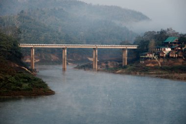 River Mountain bölgesinde ve köy yaşam tarzında dumanlı bir sabah manzarası. Gerçeküstü manzara sisli ve sis, güneşin doğuşunu yansıtan bir şekilde nehrin üzerinde yüzer. Barışçıl zen yaşamını kabul et
