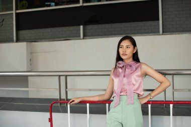 20 'li yaşlardaki Asyalı kadın portresinin yarısı düz siyah saç resmi pembe yeşil elbise giyiyor. Kadın alışveriş için dışarıda dolaşmaktan mutlu.