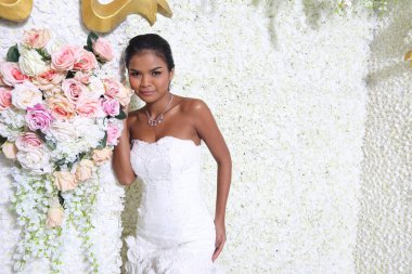 Yarı vücut, bronz tenli, Asyalı gelin beyaz gelinlik, dantel peçeli, siyah saçlı. Çiçek dekoratif duvarda mutlu bir gülümseme, stüdyo fotokopi salonu ve güzel bir stil.