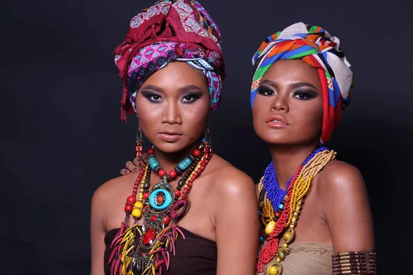 アフリカの丘の部族のスタイルを構成するファッションと20代のアジアの2人の女性の半体を閉じます 日焼けした肌の女の子は 黒の背景にカラフルな民族の付属品で強い 幸せな気持ちを表現します — ストック写真