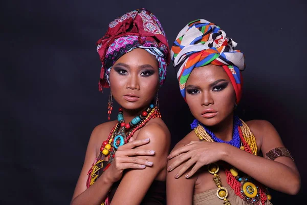 アフリカの丘の部族のスタイルを構成するファッションと20代のアジアの2人の女性の半体を閉じます 日焼けした肌の女の子は 黒の背景にカラフルな民族の付属品で強い 幸せな気持ちを表現します — ストック写真