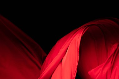 Kıvrımlı uçan kırmızı pamuk kumaş parçası, havaya düşen kırmızı pamuk parçası. Siyah arkaplan izole, koyu gölgeleme ortamı