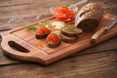 Tahtada siyah ekmek, dereotu ve limon olan kırmızı havyar.