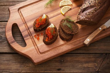 Tahtada siyah ekmek, dereotu ve limon olan kırmızı havyar.