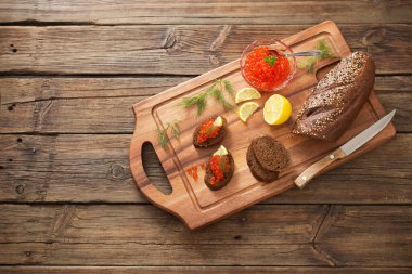 Tahtada siyah ekmek, dereotu ve limon olan kırmızı havyar.