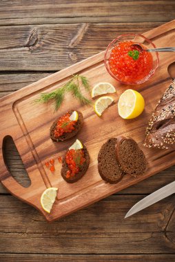 Tahtada siyah ekmek, dereotu ve limon olan kırmızı havyar.