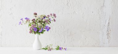 Beyaz arkaplanda beyaz vazodaki yabani çiçekler