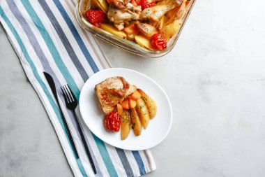 Patates, domates, havuç ve yabani otlarla pişirilmiş tavuk parçaları. Üst manzara, arka planda yan görünüm. Yakın plan ve orta plan. Metin için boşluk.