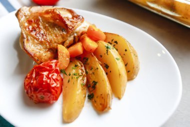 Patates, domates, havuç ve yabani otlarla pişirilmiş tavuk parçaları. Üst manzara, arka planda yan görünüm. Yakın plan ve orta plan. Metin için boşluk.