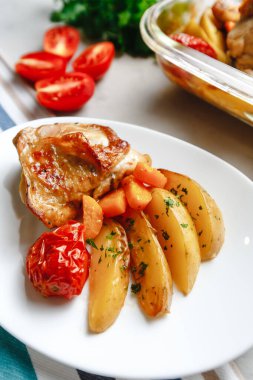 Patates, domates, havuç ve yabani otlarla pişirilmiş tavuk parçaları. Üst manzara, arka planda yan görünüm. Yakın plan ve orta plan. Metin için boşluk.