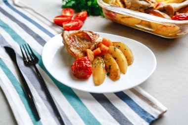 Patates, domates, havuç ve yabani otlarla pişirilmiş tavuk parçaları. Üst manzara, arka planda yan görünüm. Yakın plan ve orta plan. Metin için boşluk.