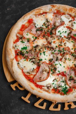 Jambonlu ve mantarlı ev yapımı pizza, domates sosu, mozzarella peyniri ve koyu arkaplanda otlar. Üst görünüm, yan görünüm