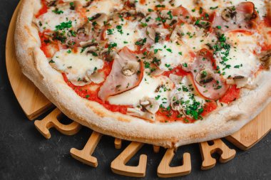 Jambonlu ve mantarlı ev yapımı pizza, domates sosu, mozzarella peyniri ve koyu arkaplanda otlar. Üst görünüm, yan görünüm