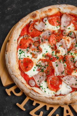 Jambonlu, sucuklu, pastırmalı, füme sosisli ve koyu otlu ev yapımı pizza. Üst görünüm, yan görünüm
