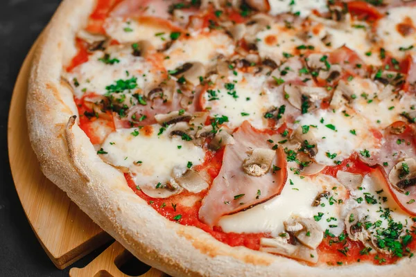 Jambonlu ve mantarlı ev yapımı pizza, domates sosu, mozzarella peyniri ve koyu arkaplanda otlar. Üst görünüm, yan görünüm
