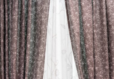 Oturma odasının camında kahverengi desenli perdeler ve beyaz tül var..