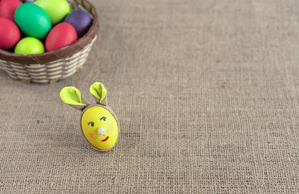 Yellow egg in the shape of an Easter bunny and multicolored eggs in a wicker basket.