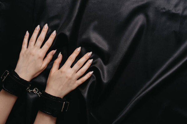 женские руки в наручниках на темном шелковом полотне