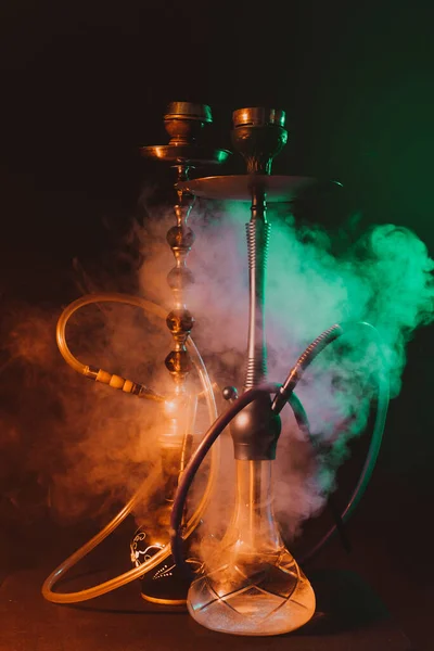 Modern hookah, shisha on a smoky black background with colored lighting and smoke — Stock Photo, Image