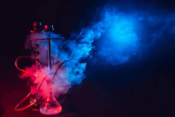 Modern hookah, shisha on a smoky black background with neon lighting and smoke. Place for your text