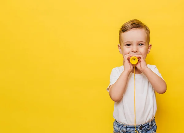 Retrato de un lindo niño riéndose sobre un fondo amarillo con un juguete en las manos. Copiar espacio. —  Fotos de Stock
