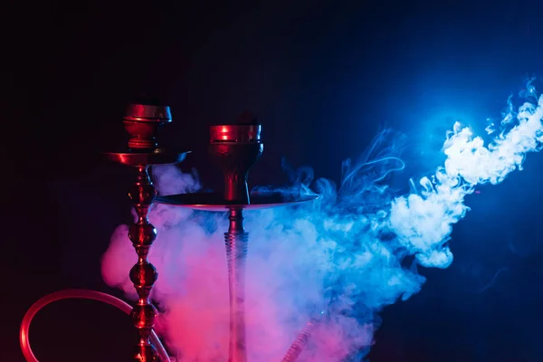 Nowoczesny hookah, shisha na dymiącym czarnym tle z kolorowym oświetleniem i dymem. Zamknij się. — Zdjęcie stockowe