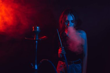 Model kız nargile içiyor, Sheesha. Kız zevkle nefes veriyor. Renk ışığı