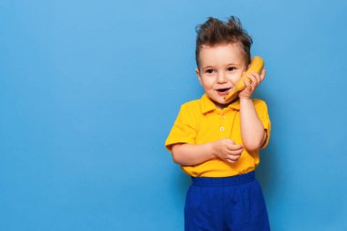 Muzlu komik surat. Sarı tişörtlü bir çocuk elinde gülümsemeli bir muz tutuyor. Komik ifadeler. Beslenme kavramı. Taze muz. Sarı stil. Mavi arkaplan