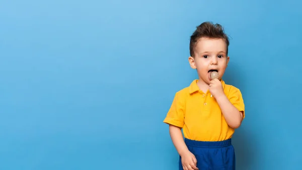 Niño con piruleta está de pie sobre un fondo de pared azul. Prevención de la caries infantil. Copiar espacio —  Fotos de Stock