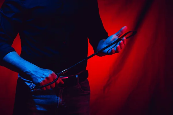 Kırmızı arka planda kırbaç tutan seksi bir adam.