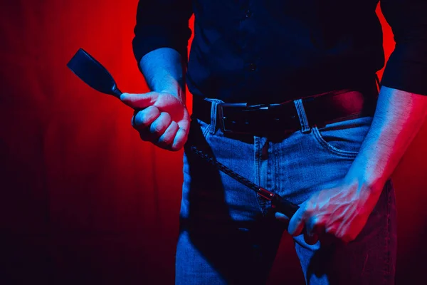 Kırmızı arka planda kırbaç tutan seksi bir adam.