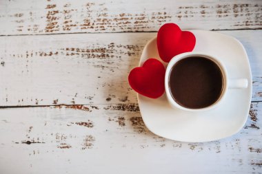Kırmızı kalpler ve beyaz ahşap arka planda bir fincan kahve..
