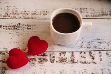 Kırmızı kalpler ve beyaz ahşap arka planda bir fincan kahve..
