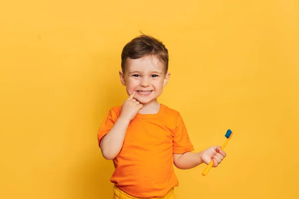 Menino bebê feliz escovando os dentes com uma escova de dentes em um fundo amarelo. Saúde, higiene oral. — Fotografia de Stock