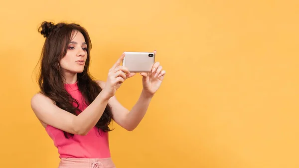 Selfie, uma linda garota tirando fotos de si mesma em seu telefone. Num fundo amarelo. instagram — Fotografia de Stock