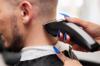 Bir kadın berber kırpıcı ile genç bir adamın saçını kesiyor. Yakın plan.