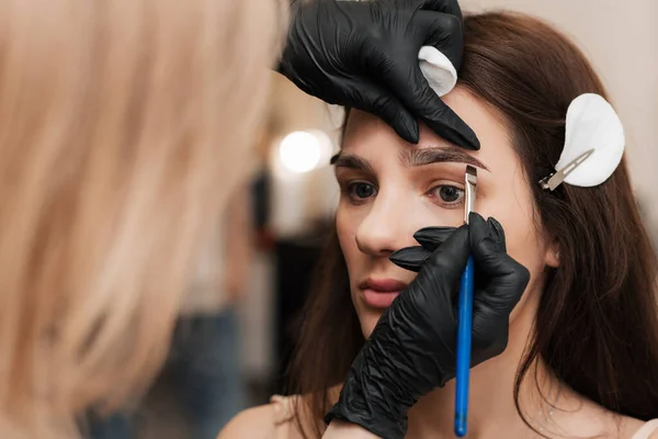 O esteticista-brovista dá forma aplicando henna com uma escova, colorindo as sobrancelhas em um salão de beleza. Cuidados faciais profissionais — Fotografia de Stock