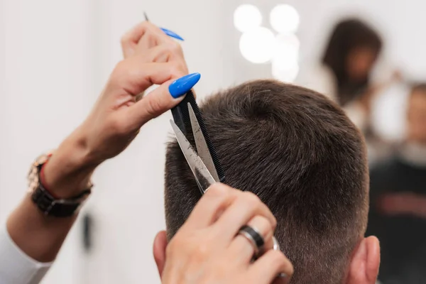 Uma barbeiro fêmea faz um corte de cabelo para um jovem com tesoura. Close-up — Fotografia de Stock