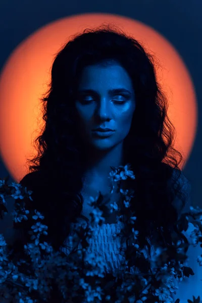 Portret dziewczyny wyglądającej jak nimfa, w neonowym oświetleniu z aureolą na głowie i kwiatami w rękach. Koncepcja fantazji, bajek, fantasmagorii. — Zdjęcie stockowe